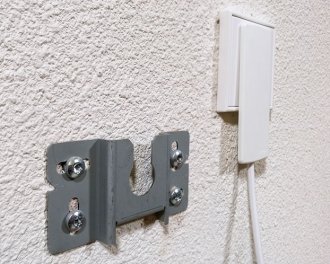 De platte stekker past in een stopcontact dat achter het infraroodpaneel verwerkt is. Links een van de twee montagebeugels De platte stekker past in een stopcontact dat achter het infraroodpaneel verwerkt is. Links een van de twee montagebeugels